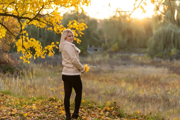 Giovane donna con foglie autunnali in mano e fondo del giardino di acero giallo autunno