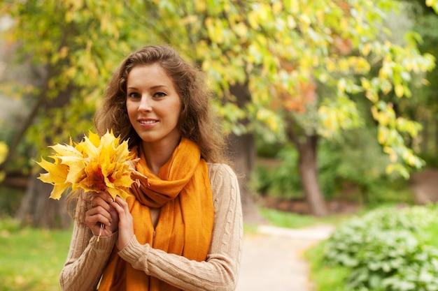 Giovane donna con foglie di autunno nel parco