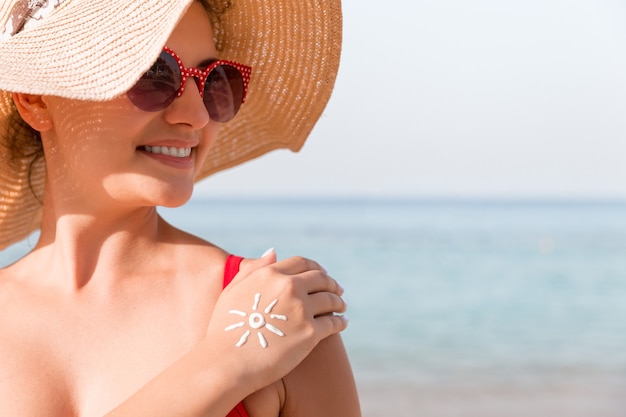 Giovane donna con forma di sole sulla sua mano fatta di crema solare in spiaggia.