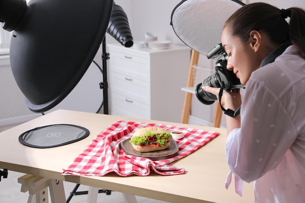 Giovane donna con fotocamera professionale che scatta foto di sandwich in studio Fotografia alimentare