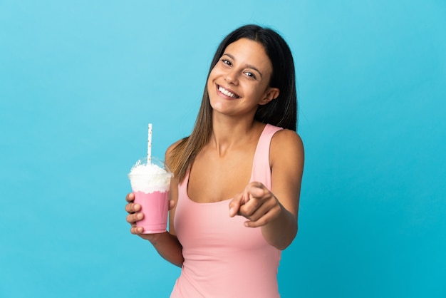 Giovane donna con frappè alla fragola che punta davanti con felice espressione