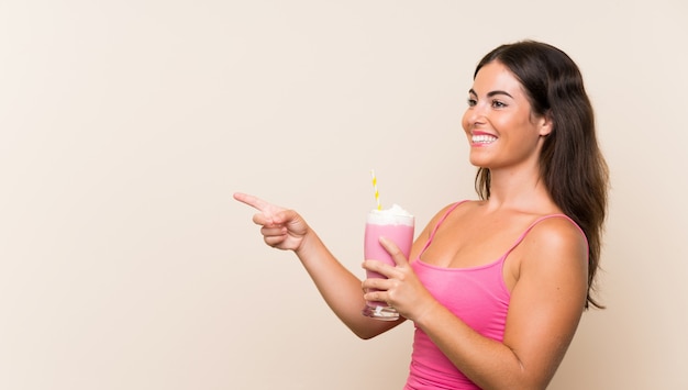 Giovane donna con frappè alla fragola che punta verso il lato per presentare un prodotto