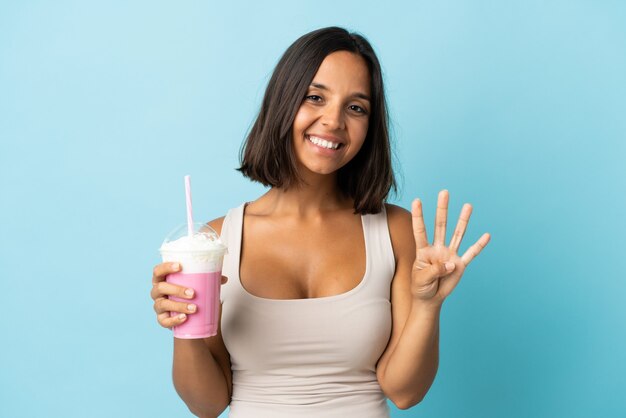 Giovane donna con frappè alla fragola isolato su sfondo blu felice e contando quattro con le dita