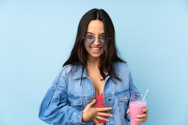 Giovane donna con frappè alla fragola isolato su sfondo blu sorridente molto