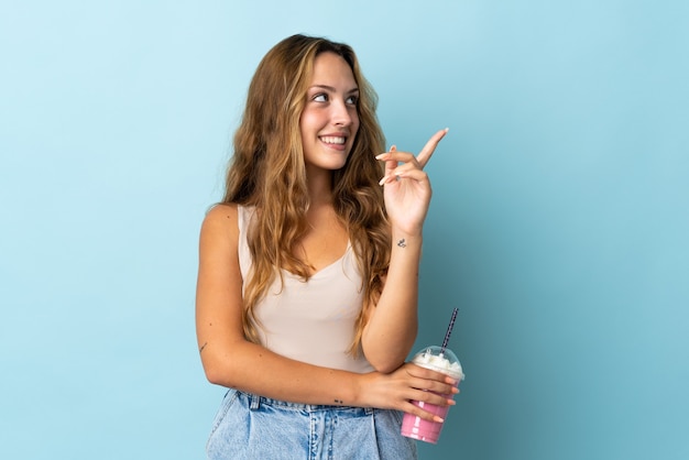 Giovane donna con frappè alla fragola isolato sulla parete blu rivolta verso l'alto una grande idea