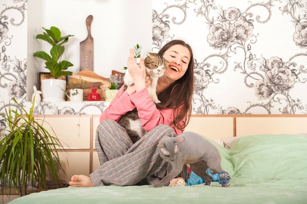 Giovane donna con gatti divertirsi in camera da letto. Resta a casa concetto.