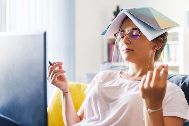 Giovane donna con gli occhi chiusi e un libro in testa seduta a casa