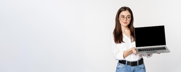 Giovane donna con gli occhiali che mostra lo schermo del laptop che mostra la promozione sul sito Web del computer o sullo standi del negozio