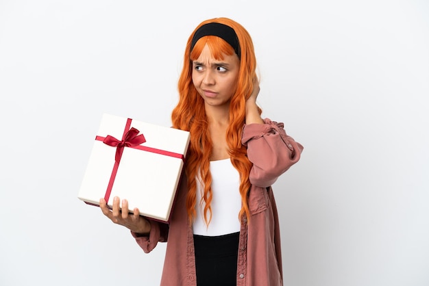 Giovane donna con i capelli arancioni in possesso di un regalo isolato su sfondo bianco avendo dubbi