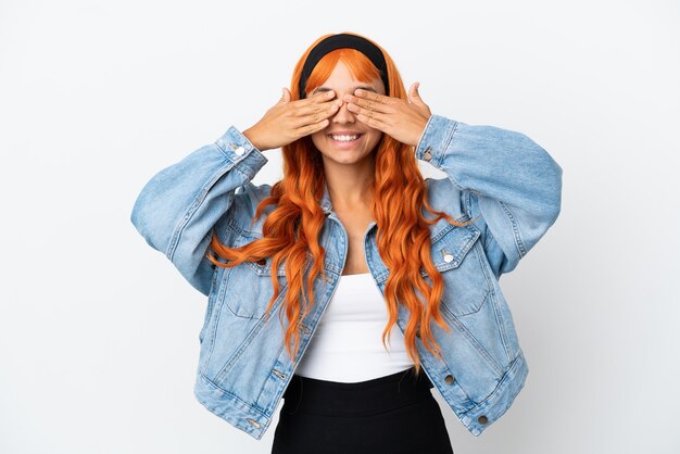 Giovane donna con i capelli arancioni isolata su sfondo bianco che copre gli occhi con le mani e sorride