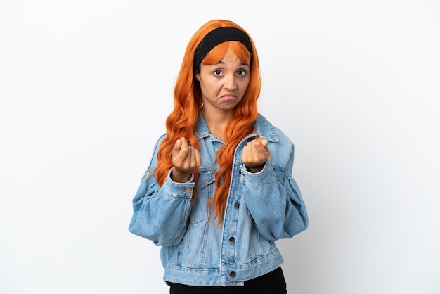 Giovane donna con i capelli arancioni isolata su sfondo bianco che fa un gesto di denaro ma è rovinata