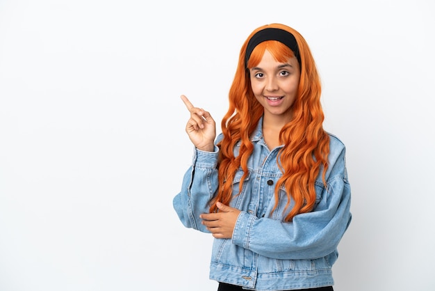 Giovane donna con i capelli arancioni isolata su sfondo bianco che punta il dito a lato