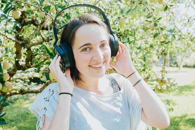 Giovane donna con i capelli corti che si diverte mentre usa un grande auricolare per ascoltare la musica. Attività esterne. La musica felice della ragazza gode.