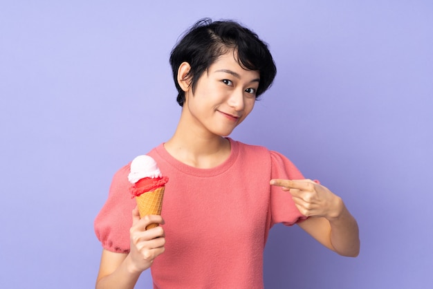 Giovane donna con i capelli corti che tiene un gelato di cornetta sopra la porpora e che lo indica