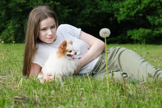 Giovane donna con i capelli lunghi giace sul prato nel parco con un cane Pomerania