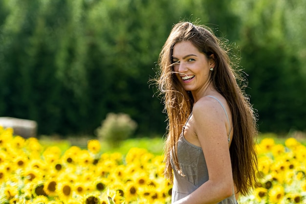 Giovane donna con i capelli lunghi in abito lineare in stile country cammina attraverso un campo di girasoli