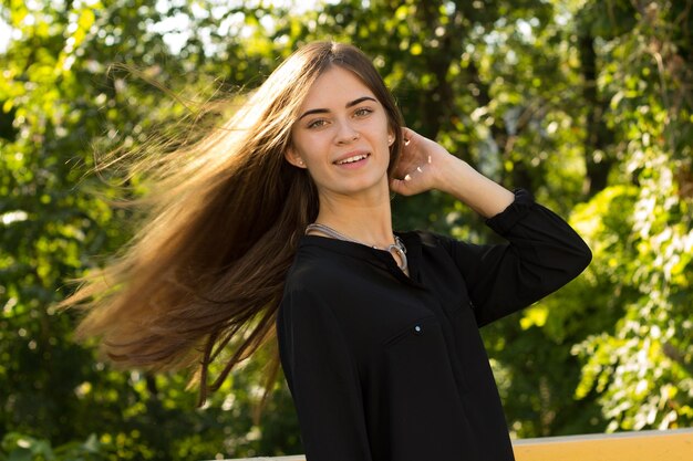 Giovane donna con i capelli lunghi in camicetta nera e collana d'argento sullo sfondo di alberi verdi