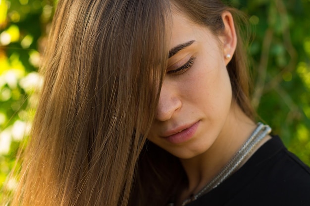 Giovane donna con i capelli lunghi in camicetta nera e collana d'argento sullo sfondo di alberi verdi