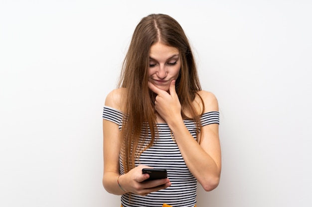 Giovane donna con i capelli lunghi sopra isolato muro bianco pensando e inviando un messaggio