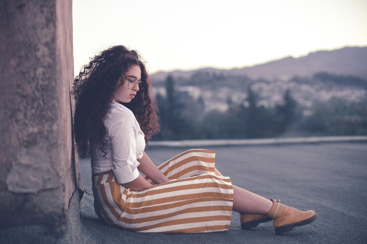 Foto giovane donna con i capelli ricci che guarda lontano mentre è seduta all'aperto