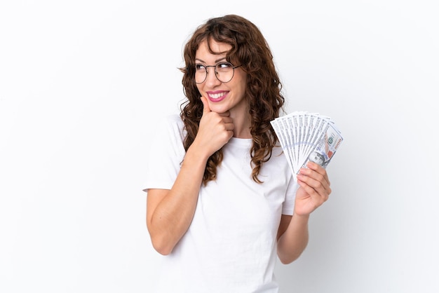 Giovane donna con i capelli ricci che prende un sacco di soldi isolato sfondo su sfondo bianco guardando al lato e sorridente