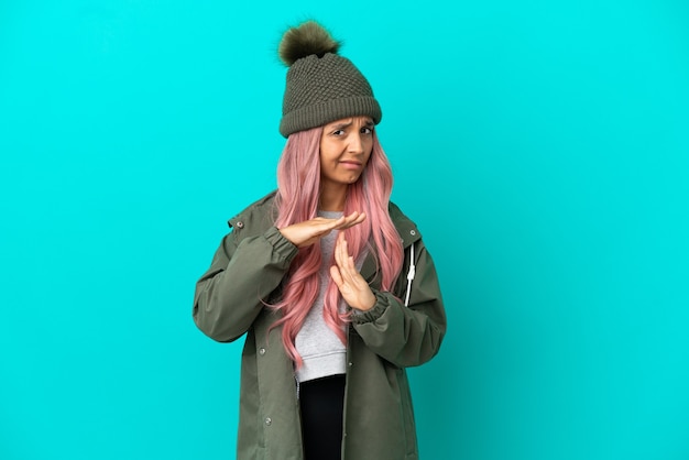 Giovane donna con i capelli rosa che indossa un cappotto antipioggia isolato su sfondo blu facendo un gesto di time out