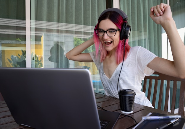 Giovane donna con i capelli rosa che lavora con il computer portatile nel caffè o terrazza di casa