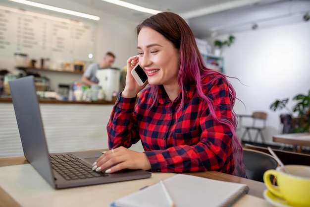 Giovane donna con i capelli rosa con il computer portatile seduto al caffè studentessa intelligente che lavora o...