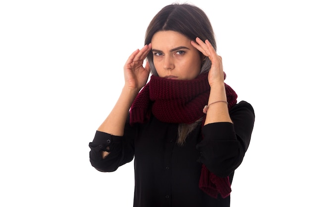 Giovane donna con i capelli scuri con una lunga sciarpa che ha un brutto mal di testa su sfondo bianco in studio