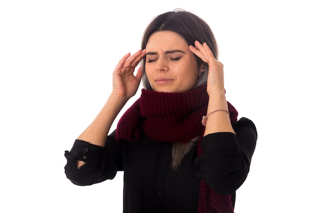 Giovane donna con i capelli scuri in camicetta nera con sciarpa lunga che ha un forte mal di testa su sfondo bianco in studio