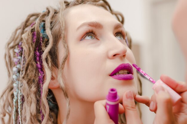 Giovane donna con i dreadlocks dipinge le labbra con il rossetto