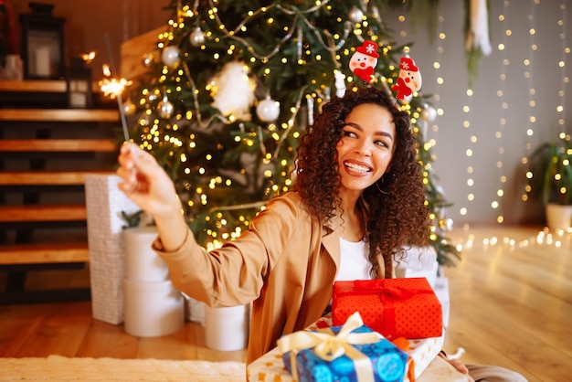 Giovane donna con i regali di Natale a casa vicino all'albero di Natale Vacanze invernali Capodanno