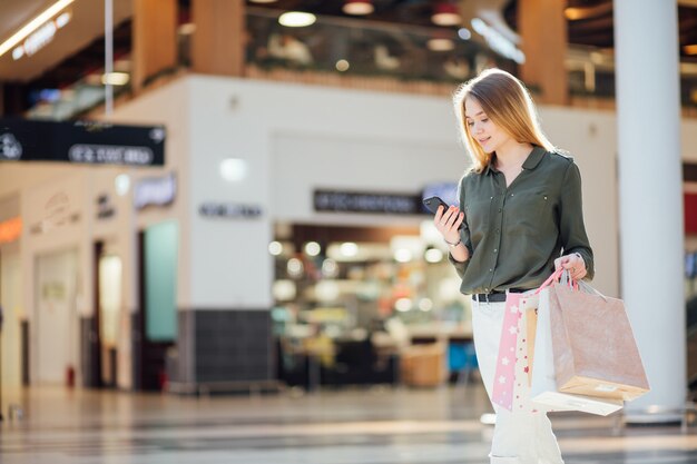 Giovane donna con i sacchetti della spesa facendo uso del suo Smart Phone per acquistare