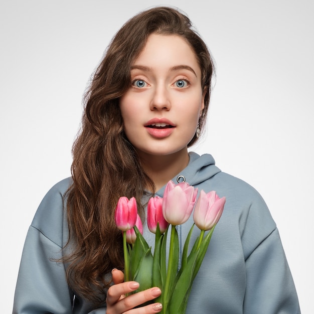 Giovane donna con i tulipani. Occhi azzurri, capelli lunghi e sorpresa sul viso.