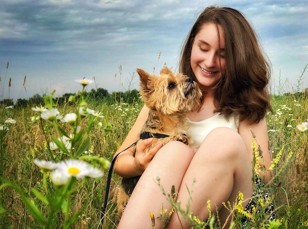 Giovane donna con il cane sul campo contro il cielo