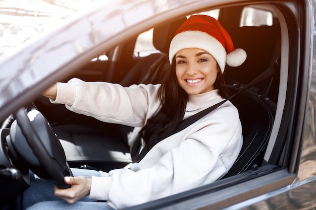 Giovane donna con il cappello di Babbo Natale alla guida della sua auto