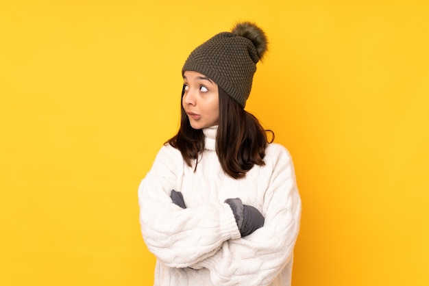 Giovane donna con il cappello di inverno sopra la parete gialla isolata con l'espressione confusa del fronte