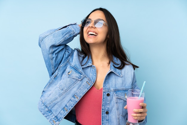 Giovane donna con il frappè alla fragola sul blu isolato che sorride molto