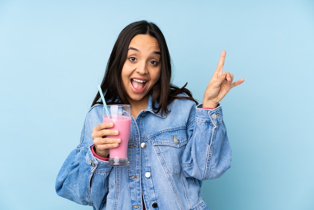 Giovane donna con il frappè alla fragola sulla parete blu isolata che indica il dito ai laterali e felice