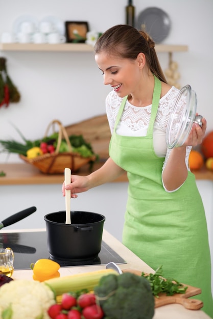 Giovane donna con il grembiule verde che cucina in cucina La casalinga sta preparando la zuppa