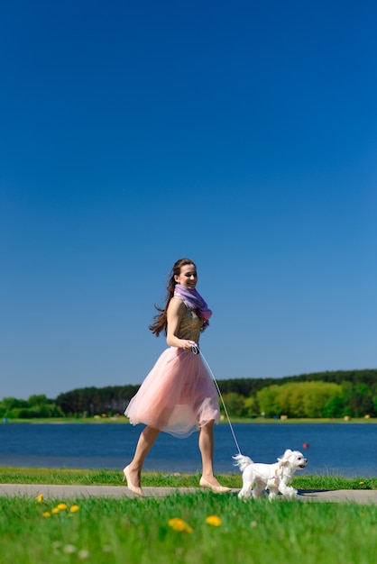 Giovane donna con il suo cane. Il cucciolo di cane bianco corre con il suo proprietario. Concetto di amicizia, animale e libertà.