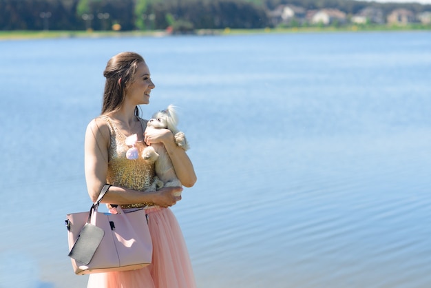 Giovane donna con il suo cane. Il cucciolo di cane bianco corre con il suo proprietario. Concetto di amicizia e animale.