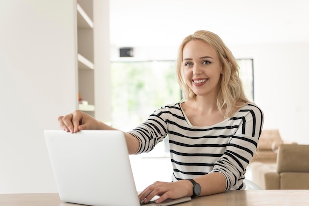 Giovane donna con il suo computer portatile nella sua lussuosa casa moderna, sorridente