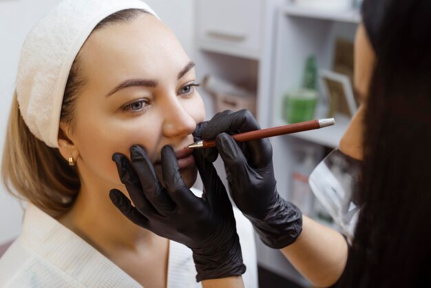 Giovane donna con il trucco permanente sulle labbra in un disegno del tatuaggio di trucco permanente del salone di cosmetologi