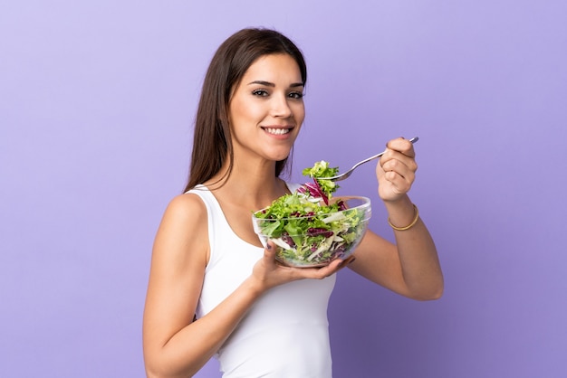 Giovane donna con insalata isolata sulla parete viola