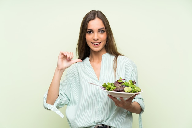 Giovane donna con insalata sopra la parete verde isolata fiera e soddisfatta di sé