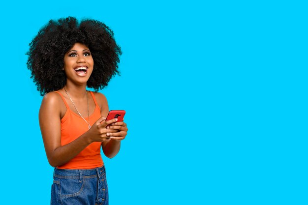 Giovane donna con l'acconciatura afro che tiene il cellulare isolato su sfondo grigio, concetto di pubblicità persona.