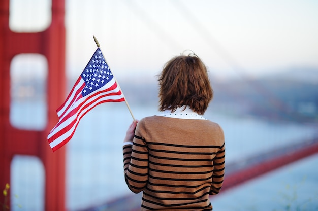 Giovane donna con la bandiera americana che considera golden gate bridge famoso a San Francisco, California, USA