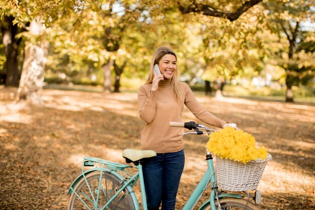 Giovane donna con la bicicletta che utilizza smartphone nel parco di autunno