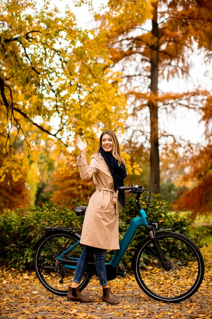 Giovane donna con la bicicletta elettrica nel parco autunnale di te